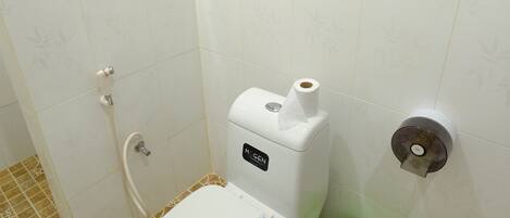 A bathroom with a toilet, a green bucket, and a paper towel dispenser.