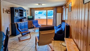 L’intérieur chaleureux d’un chalet, avec un décor en bois, un téléviseur, un canapé et un fauteuil à bascule.