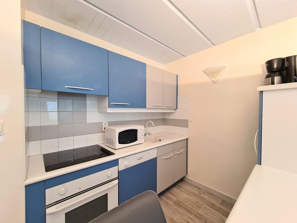 Una cocina compacta con armarios azules y blancos, un microondas, un fregadero y una estufa.