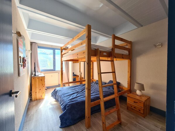 Quarto com beliche, uma escada de madeira, mesa de cabeceira com abajur e janela com cortinas.