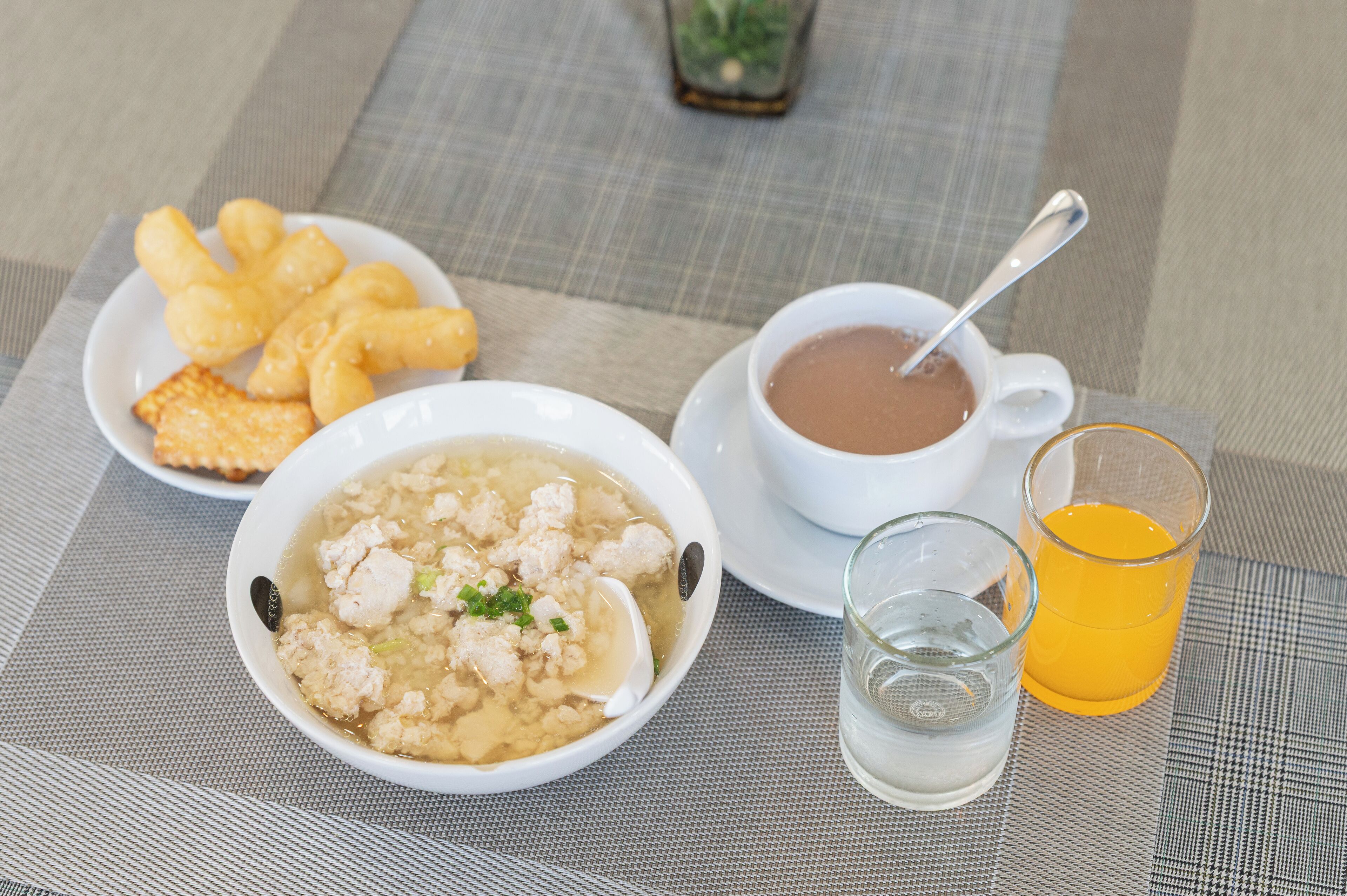 A table with a bowl of soup, a cup of tea, a glass of orange juice, and some crackers.