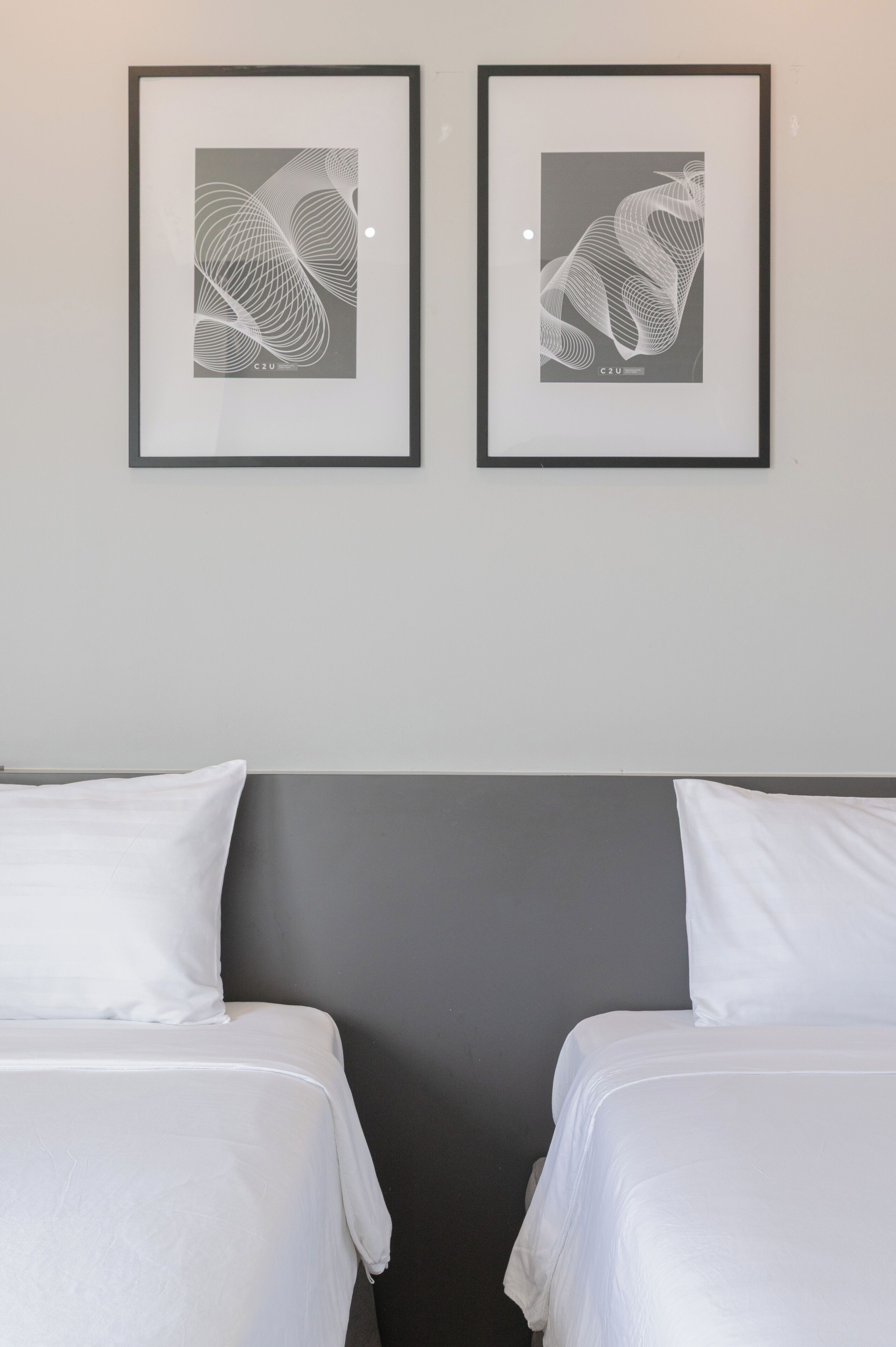 A hotel room with two beds, a grey headboard, and two framed abstract artworks on the wall.