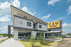 Un hotel moderno con un llamativo letrero 'C2U HOTEL', ventanas amplias y un césped bien cuidado.