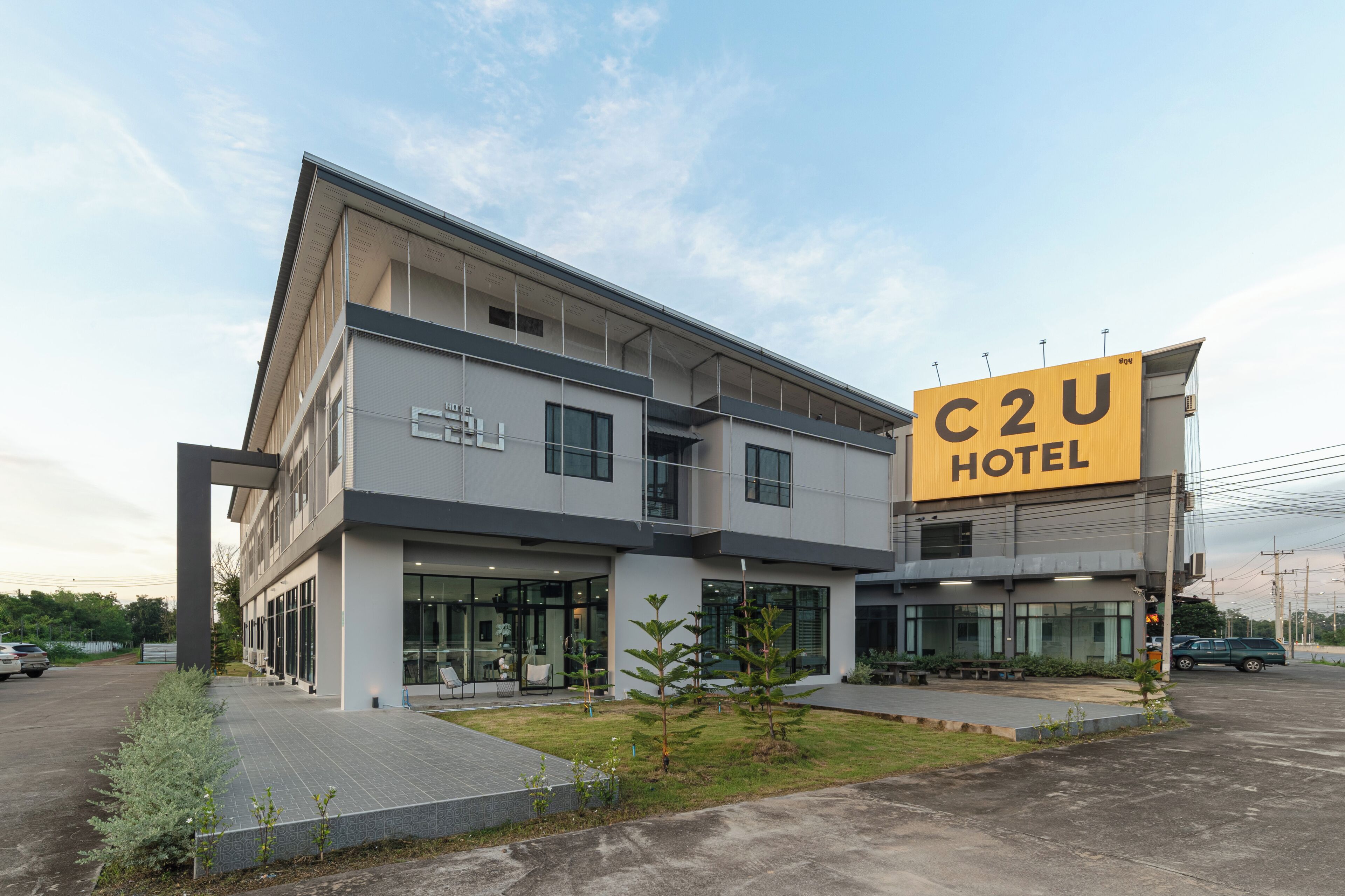 Un hôtel moderne, reconnaissable à son grand panneau C2U, doté de grandes fenêtres et d’une pelouse bien entretenue.