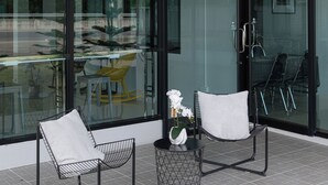 A modern outdoor seating area with two chairs and a small table, large glass windows, and a view of the street.