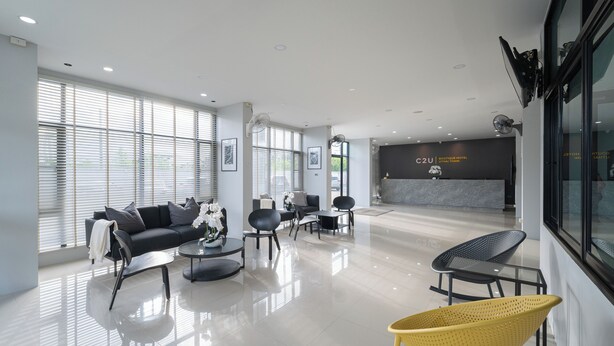 A modern hotel lobby with a black sofa, chairs, a yellow chair, and a reception desk.
