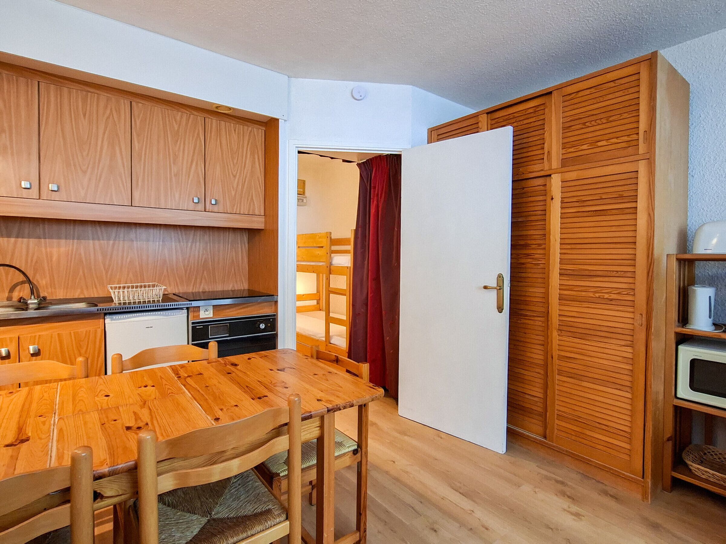 Une cuisine de taille réduite, avec des meubles de rangement en bois, une table à manger, des chaises et un rideau rouge.