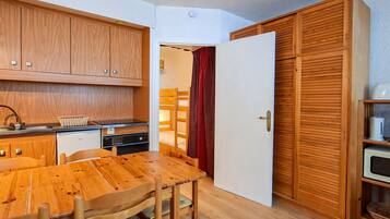 Une cuisine de taille réduite, avec des meubles de rangement en bois, une table à manger, des chaises et un rideau rouge.