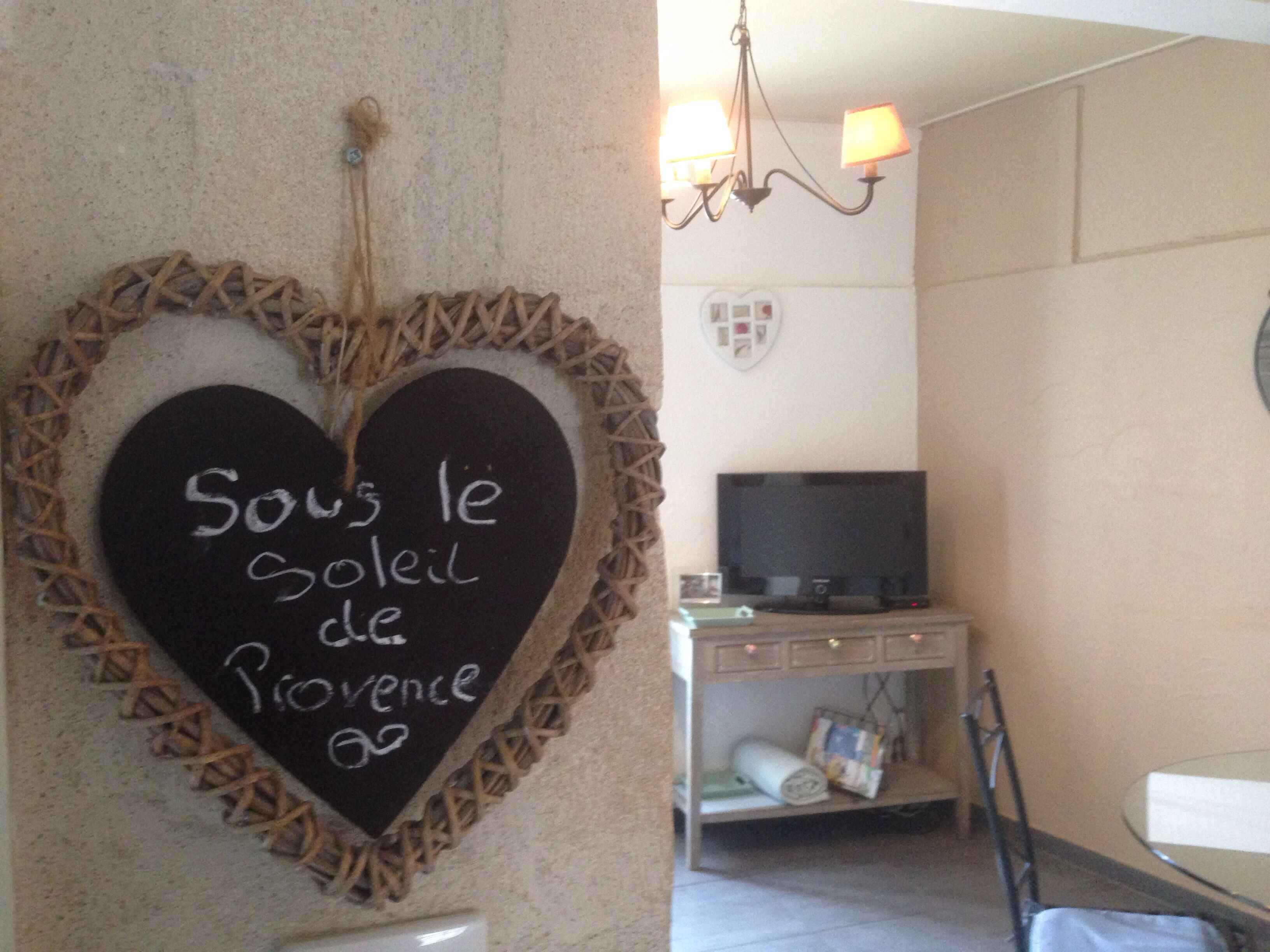 A room with a heart-shaped chalkboard on the wall, a television on a stand, and a small table with items on it.
