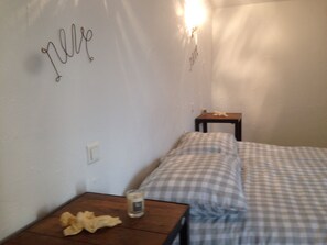 Ett sovrum med en säng, ett litet träbord, en lampa och en vägg med dekorativ text.