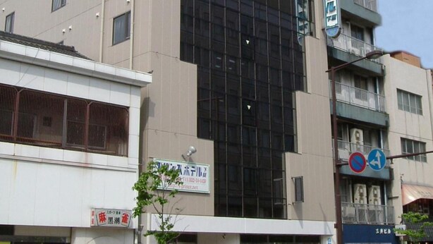 A modern building with large glass windows, a sign for a business, and a blue directional sign on the corner. - Prince Hotel Shimonoseki (Shimonoseki)