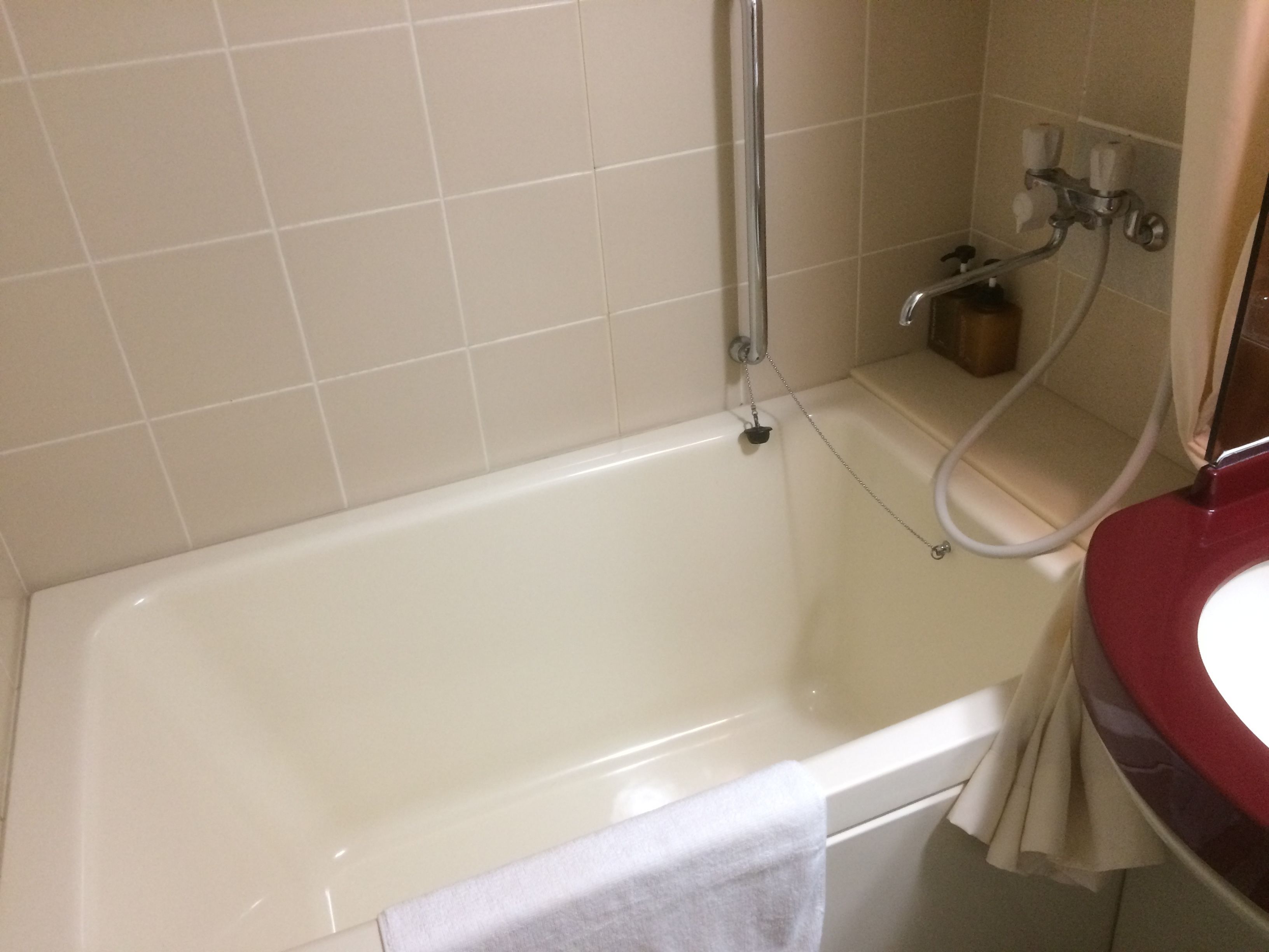 A bathroom with a white bathtub, a shower area, and a red sink.