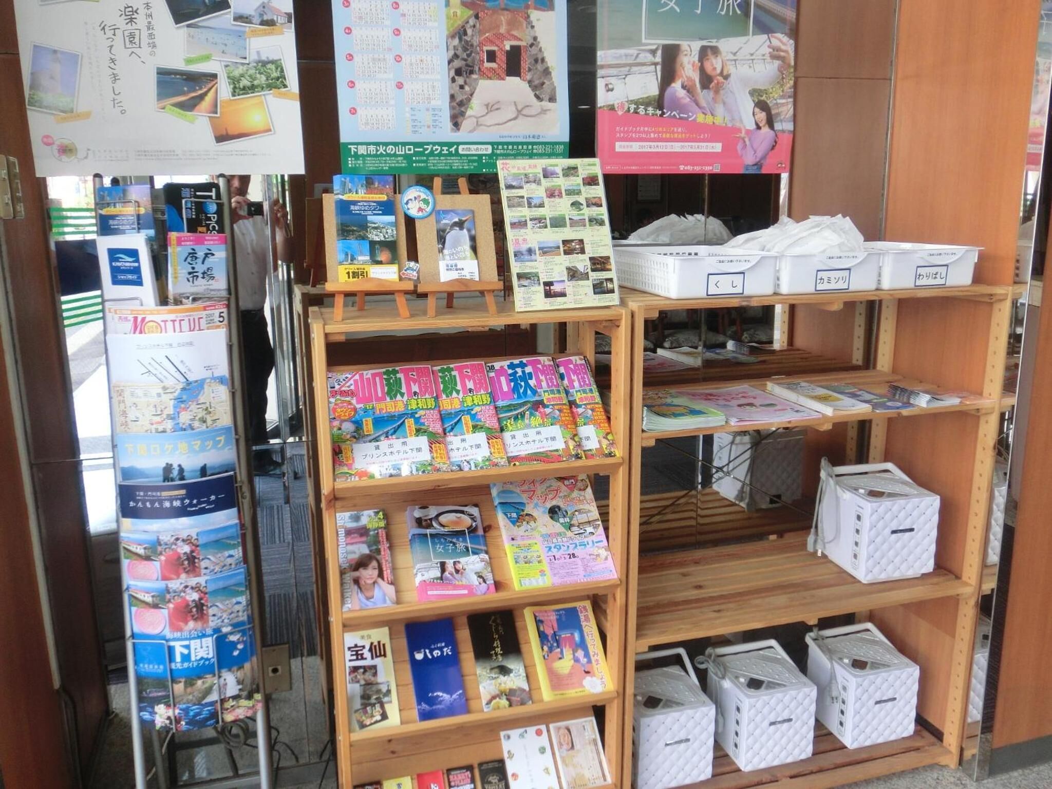 Una librería con estanterías llenas de libros y revistas, una exhibición de postales y una sección con cajas blancas.