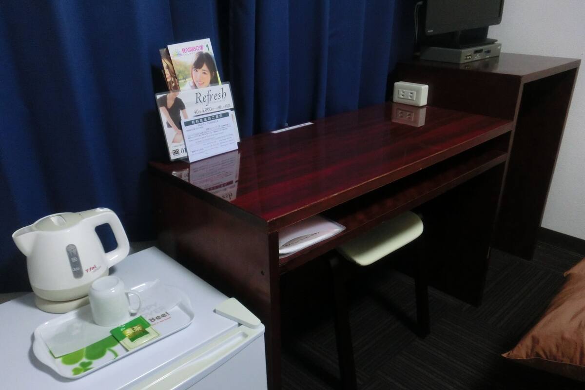 Une chambre d’hôtel avec un bureau en bois, un réfrigérateur blanc, une bouilloire, un plateau avec un sachet de thé et un panneau accroché au mur.