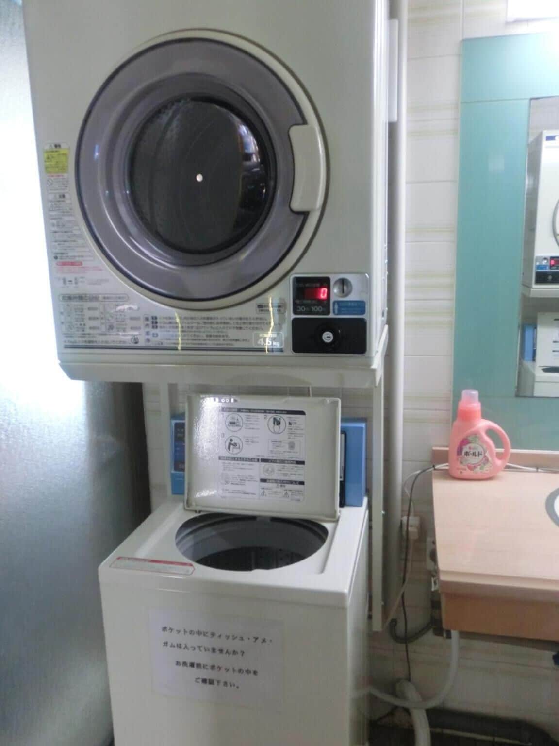 A compact, white laundry room with a front-loading washing machine, a dryer, and a small sink with a pink bottle of detergent.