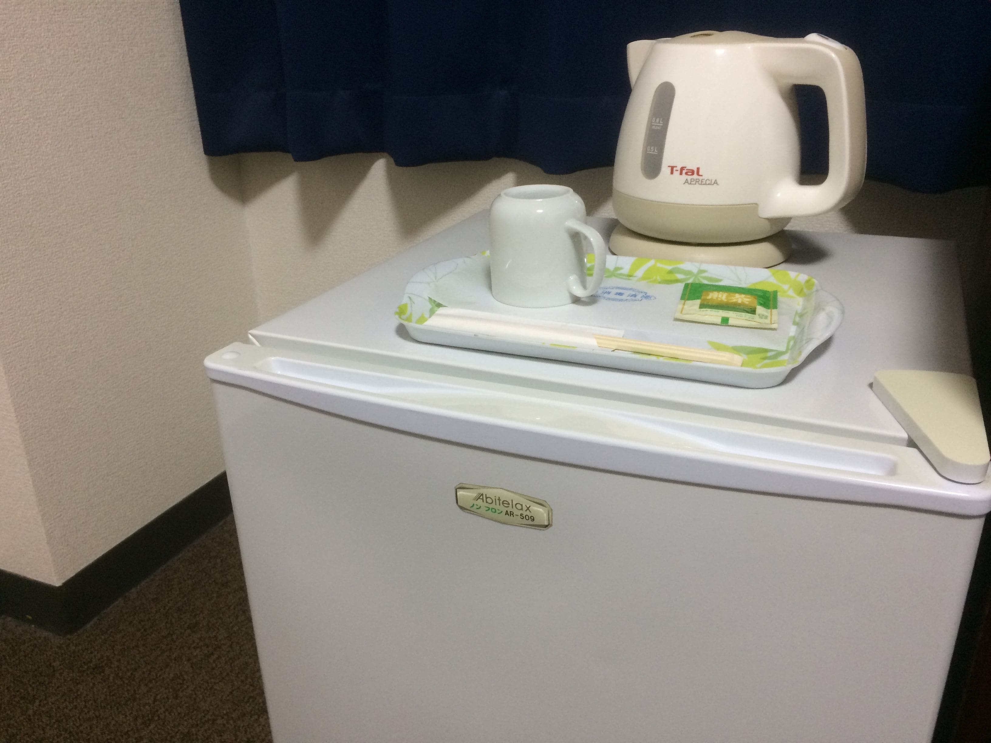 A minibar with a coffee maker, a mug, a tray with a green packet, and a soap bar.