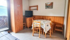 A cozy room with a wooden table and chairs, a television on a wooden cabinet, and a painting on the wall. - Bright studio in Flaine center with balcony, sleeps 4 (Flaine)