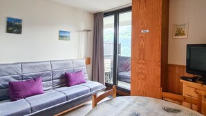 A room with a grey sofa, a wooden cabinet, a television, and a table with a patterned tablecloth. - Bright studio in Flaine center with balcony, sleeps 4 (Flaine)