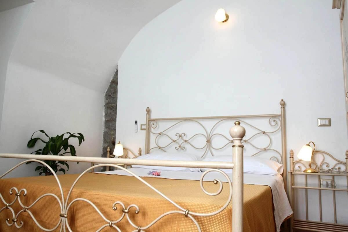 Una cama con estructura metálica y colcha color beige en una habitación con paredes blancas y un detalle de piedra.