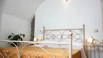 Una cama con estructura metálica y colcha color beige en una habitación con paredes blancas y un detalle de piedra.