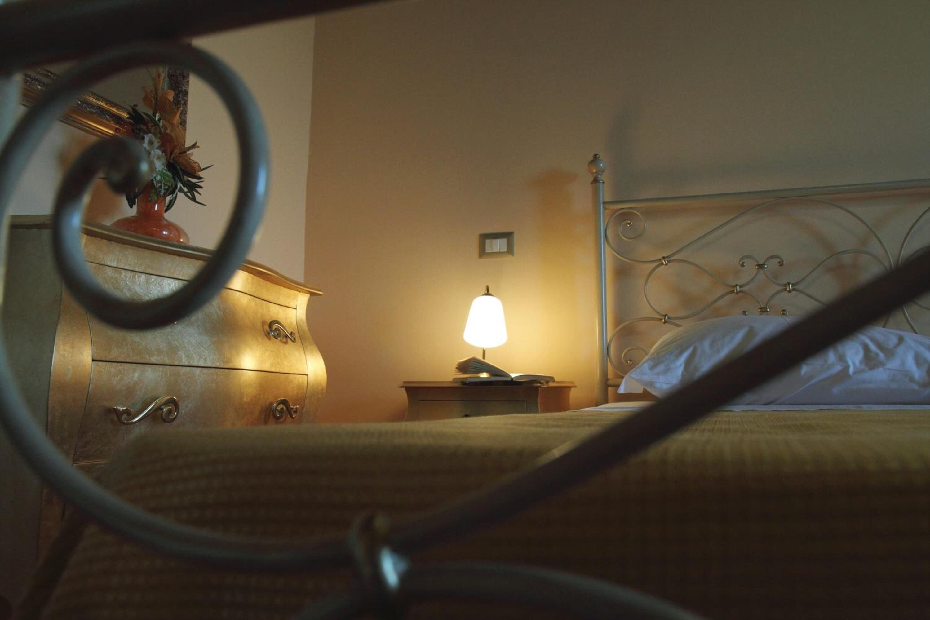 Un dormitorio con estructura de cama metálica, una mesita de noche con lámpara y un aparador con cajones.