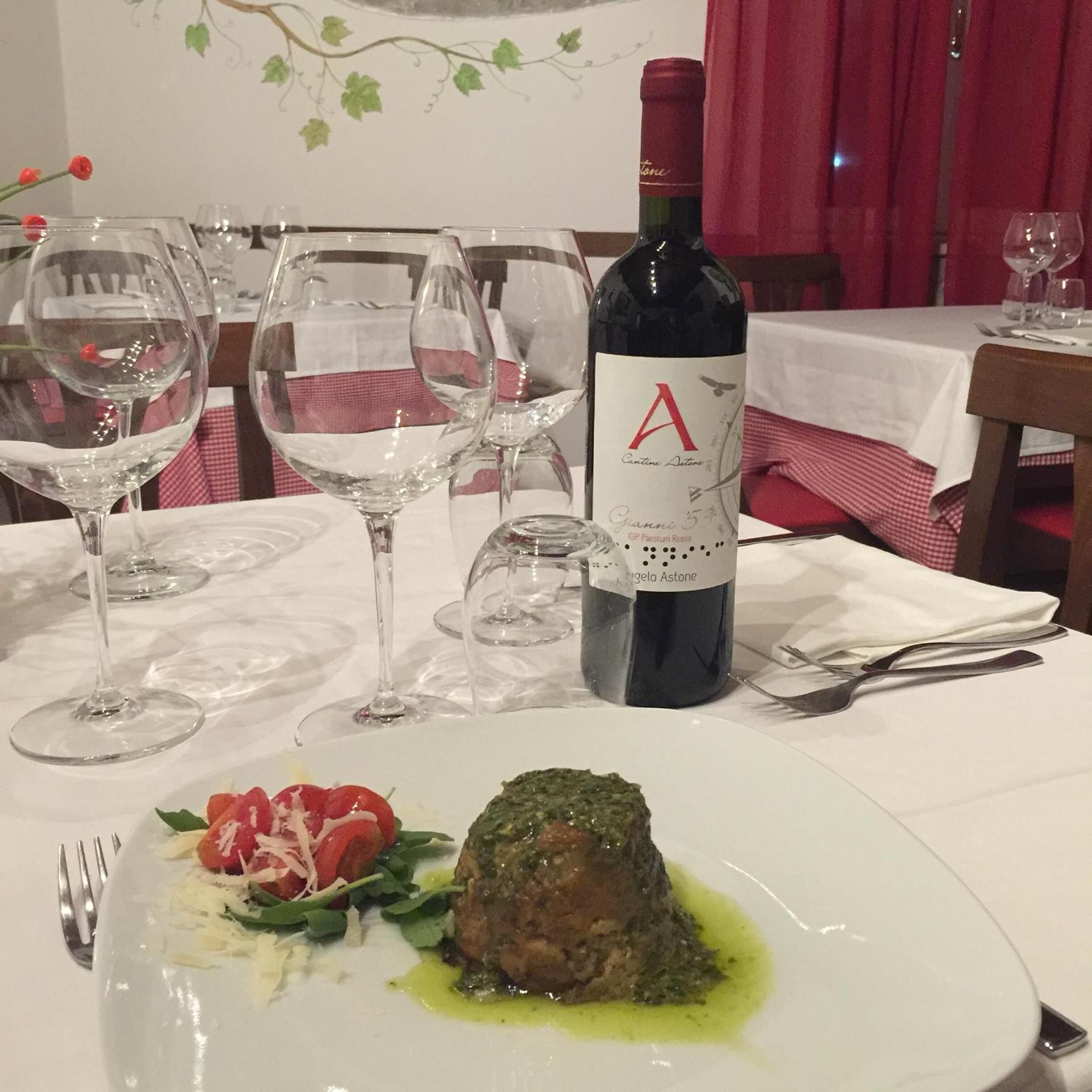 A dining table with a bottle of wine, empty wine glasses, and a plate with a meat dish and salad.