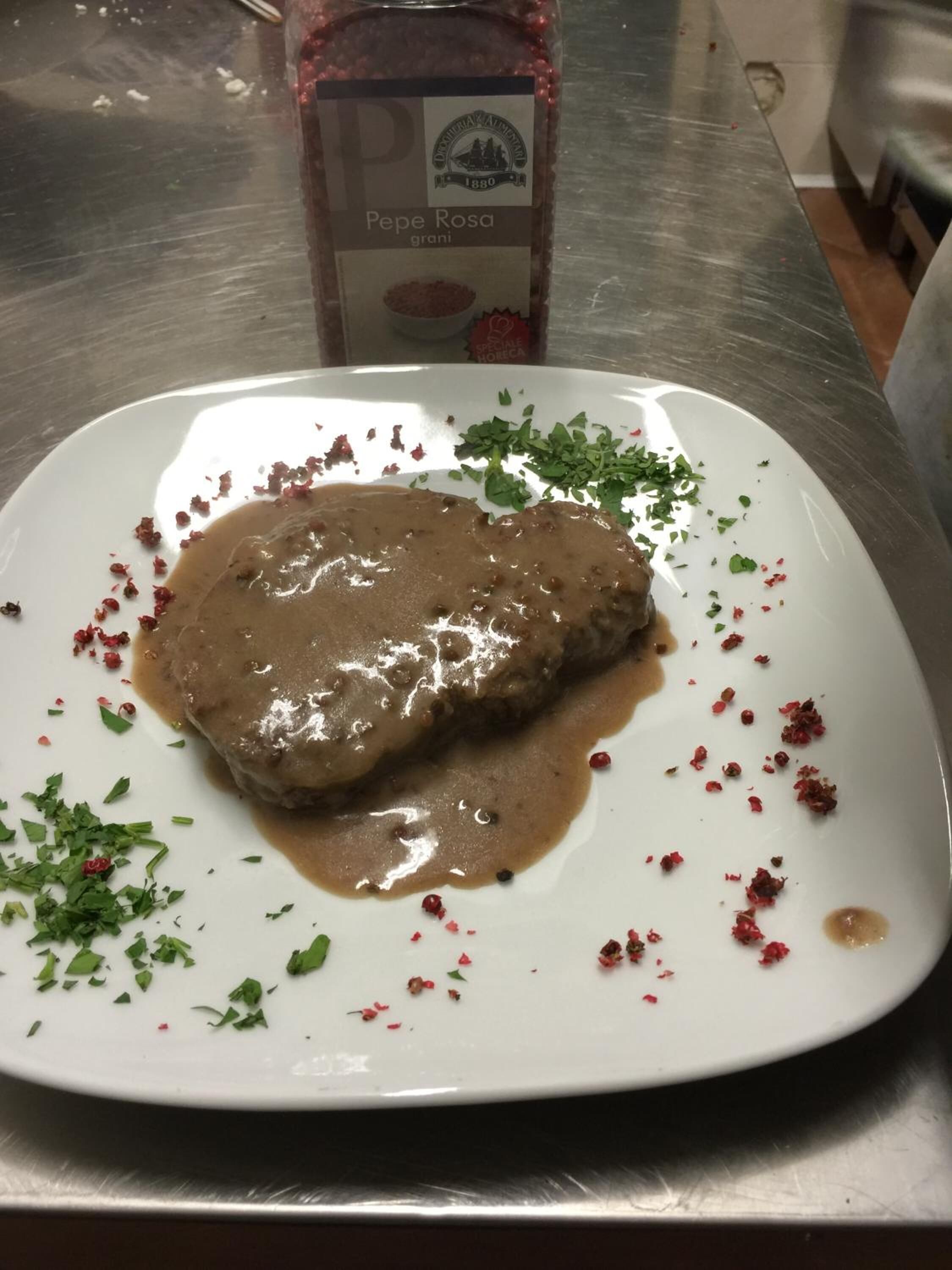 Ein Teller mit einem Fleischgericht und Soße, garniert mit Kräutern, auf einer Edelstahlplatte.