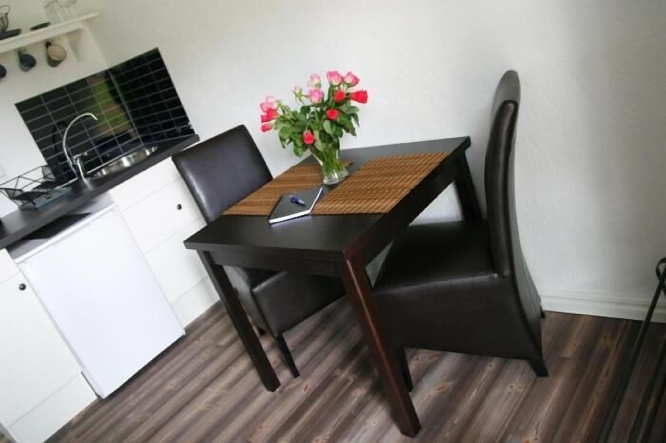 Una pequeña cocina con mesa, sillas y un jarrón de flores.