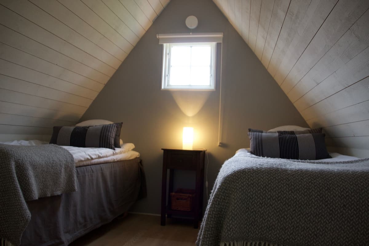Une chambre mansardée chaleureuse avec deux lits, une petite fenêtre et une table de chevet.