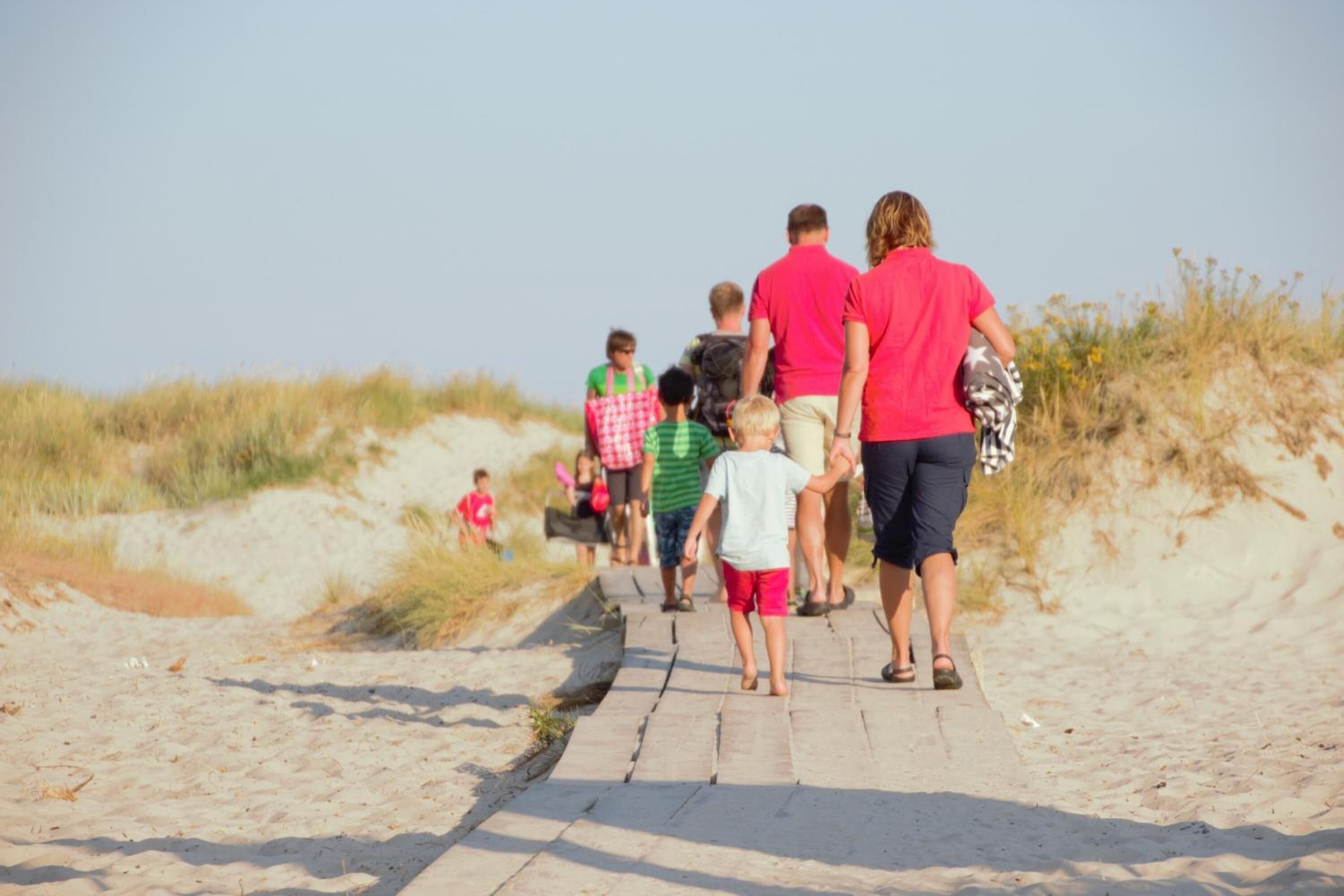 Una familia caminando por un sendero arenoso con dunas al fondo.