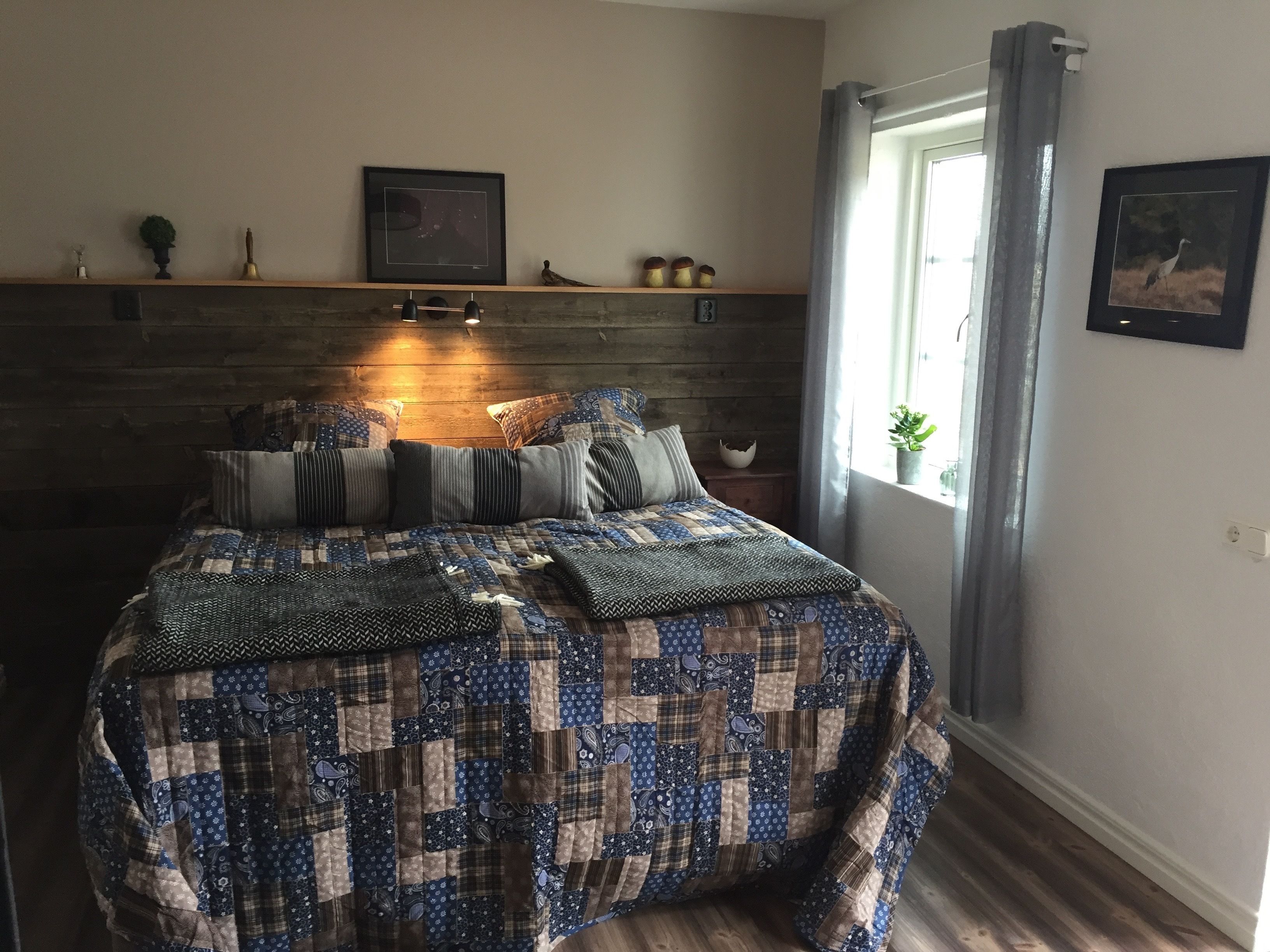 Une chambre à coucher avec une tête de lit en bois, une couvre-lit matelassée, une table de chevet avec une lampe et une fenêtre avec des rideaux.