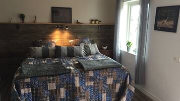 Une chambre à coucher avec une tête de lit en bois, une couvre-lit matelassée, une table de chevet avec une lampe et une fenêtre avec des rideaux.