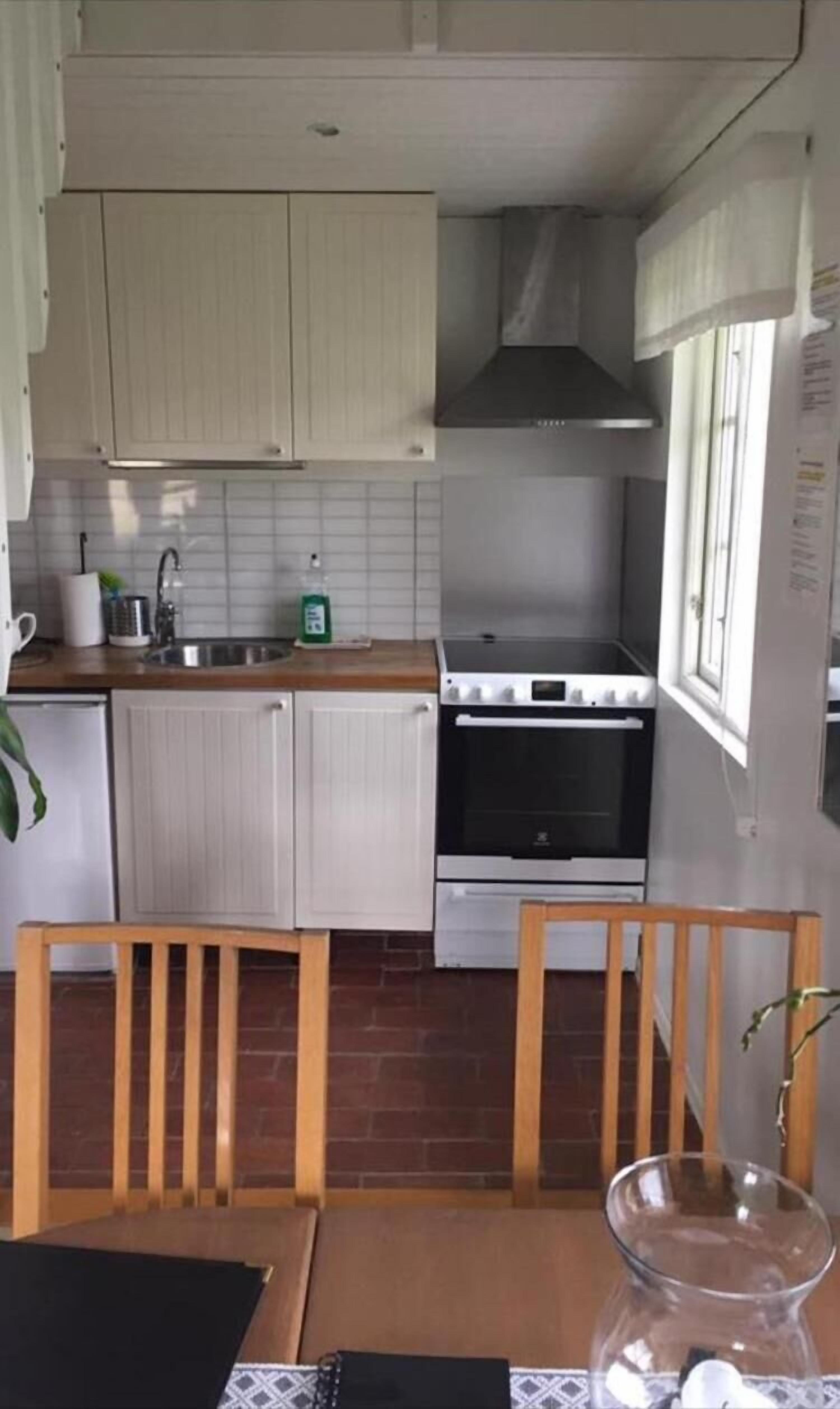 A kitchen with white cabinets, a stove, and a sink. There is a window with curtains and a plant on the counter.