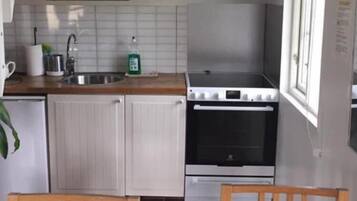 A kitchen with white cabinets, a stove, and a sink. There is a window with curtains and a plant on the counter.