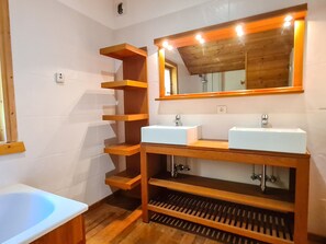 A bathroom with two sinks, wooden shelves, a mirror, and a bathtub.