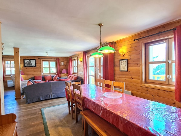 Interno accogliente di una baita con zona pranzo, pareti in legno e ampie finestre.