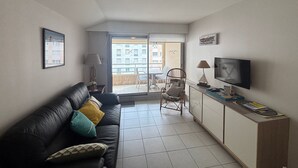 A compact living space with a sofa, a TV, and a small dining area. - Downtown Apartment Steps from Beach with Garage (Les Sables-d'Olonne)