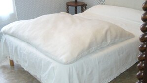 A neatly made bed with a white bedspread and pillows, a wooden nightstand with a lamp, and patterned wallpaper. - Downtown Apartment Steps from Beach with Garage (Les Sables-d'Olonne)