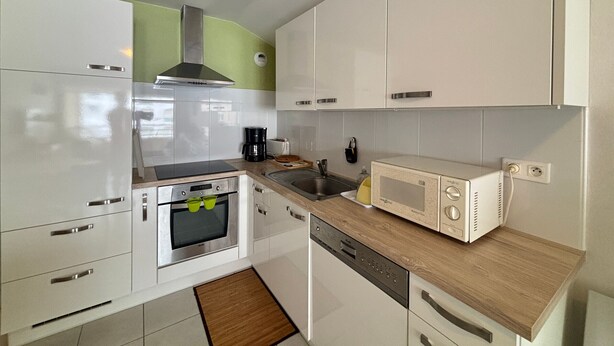 A compact kitchen with white cabinets, a stainless steel oven, a microwave, and a coffee maker. - Downtown Apartment Steps from Beach with Garage (Les Sables-d'Olonne)