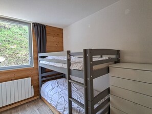 Ein Schlafraum mit Etagenbett, Fenster, Holzwand und weißem Heizkörper.
