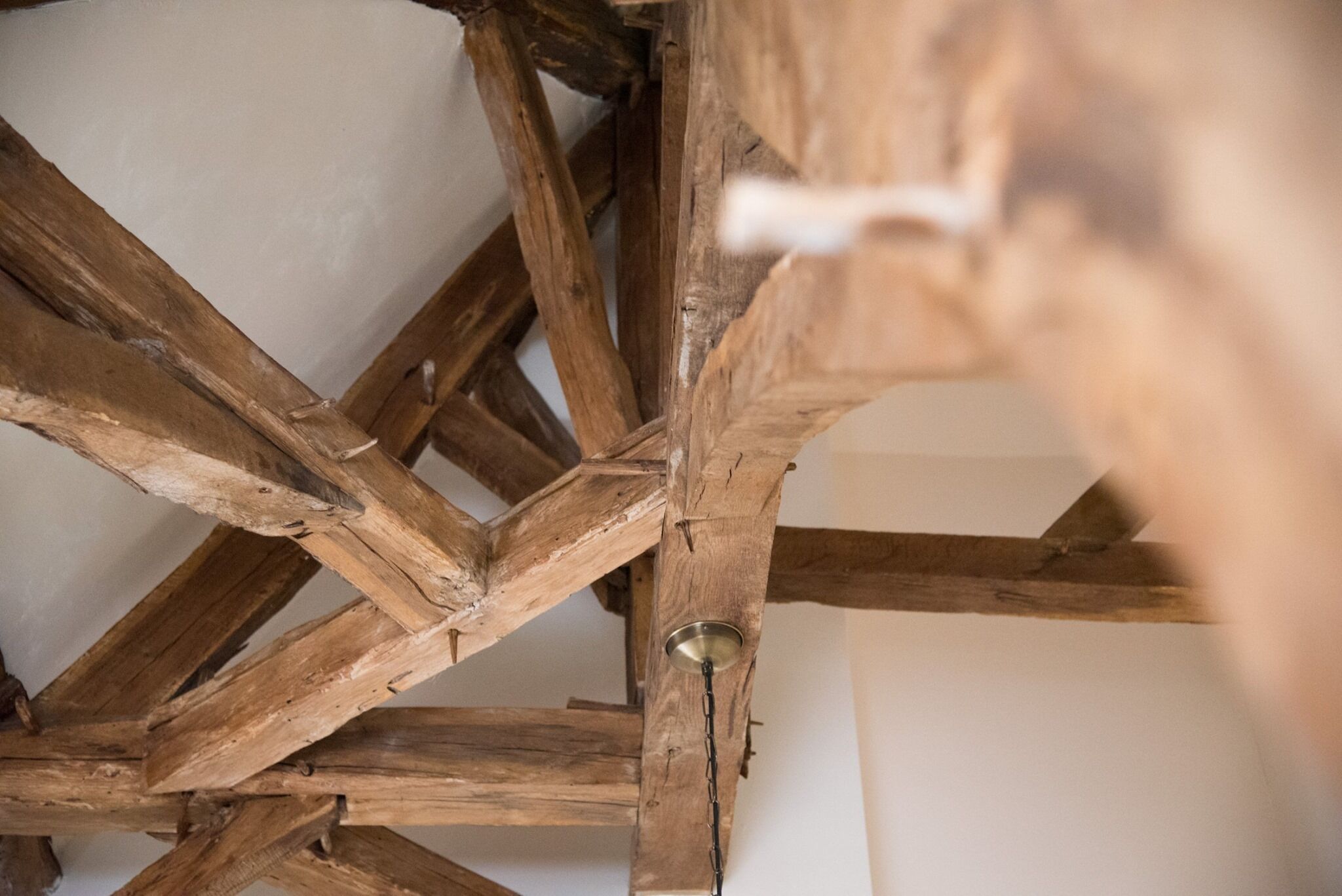 Een plafond met zichtbare houten balken en een metalen armatuur.