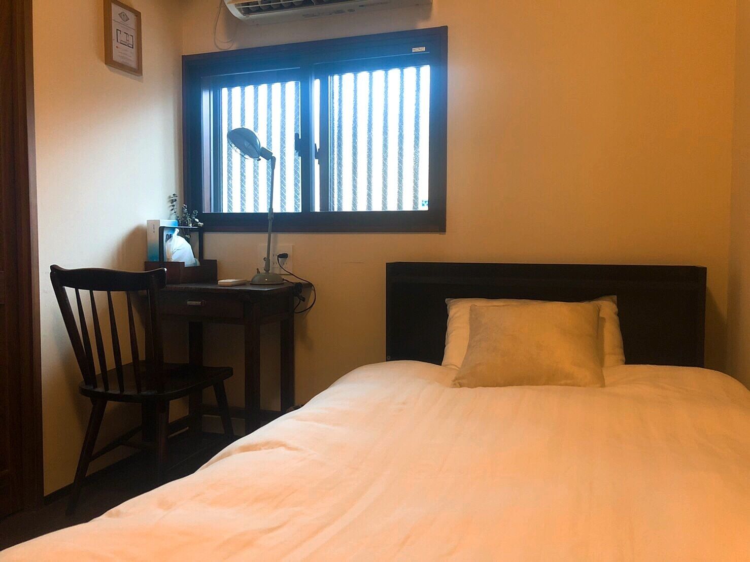 Habitación de hotel con cama, escritorio con silla, ventana con persianas y equipo de aire acondicionado.