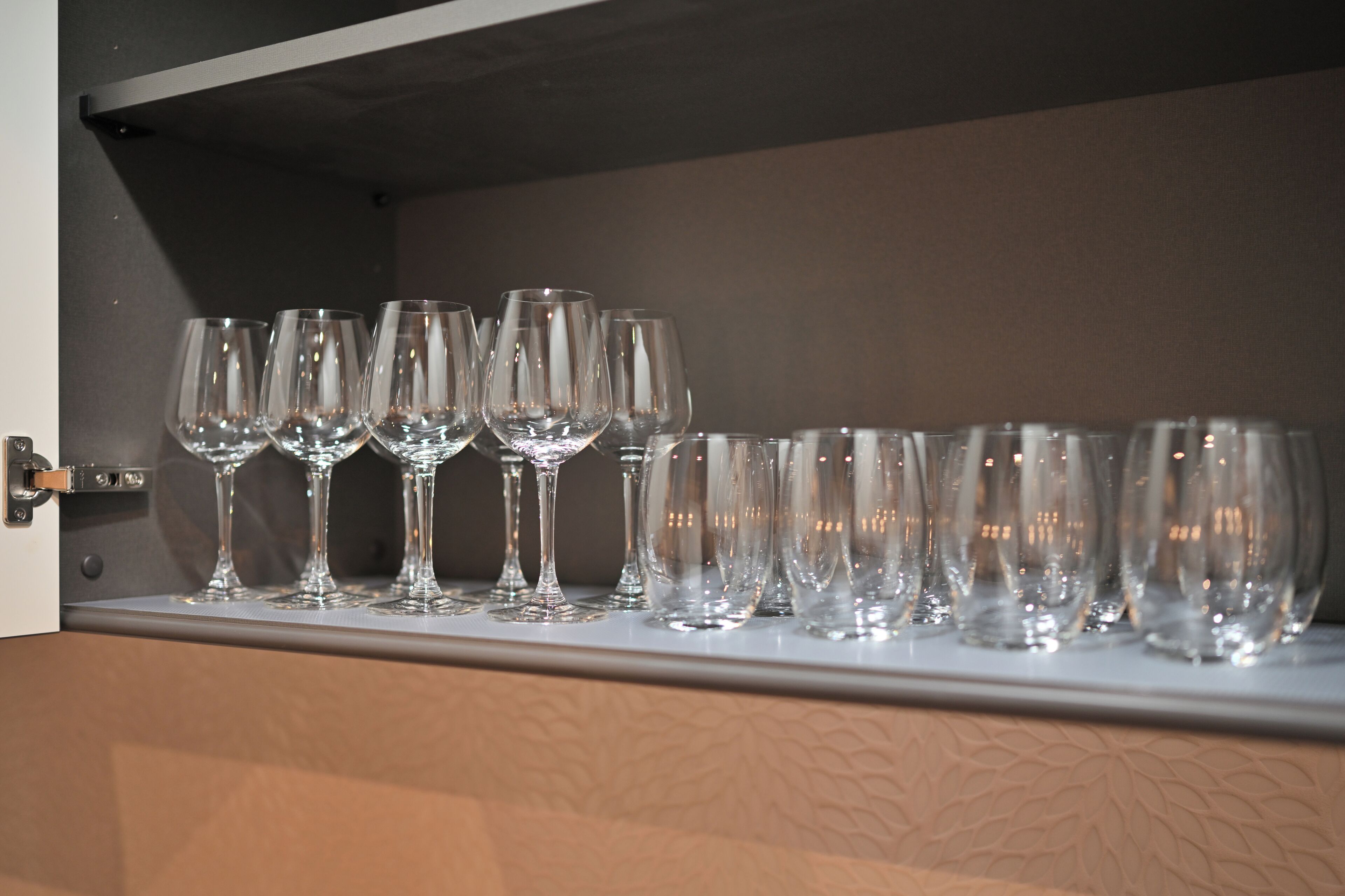 A row of empty wine glasses on a shelf inside a room.