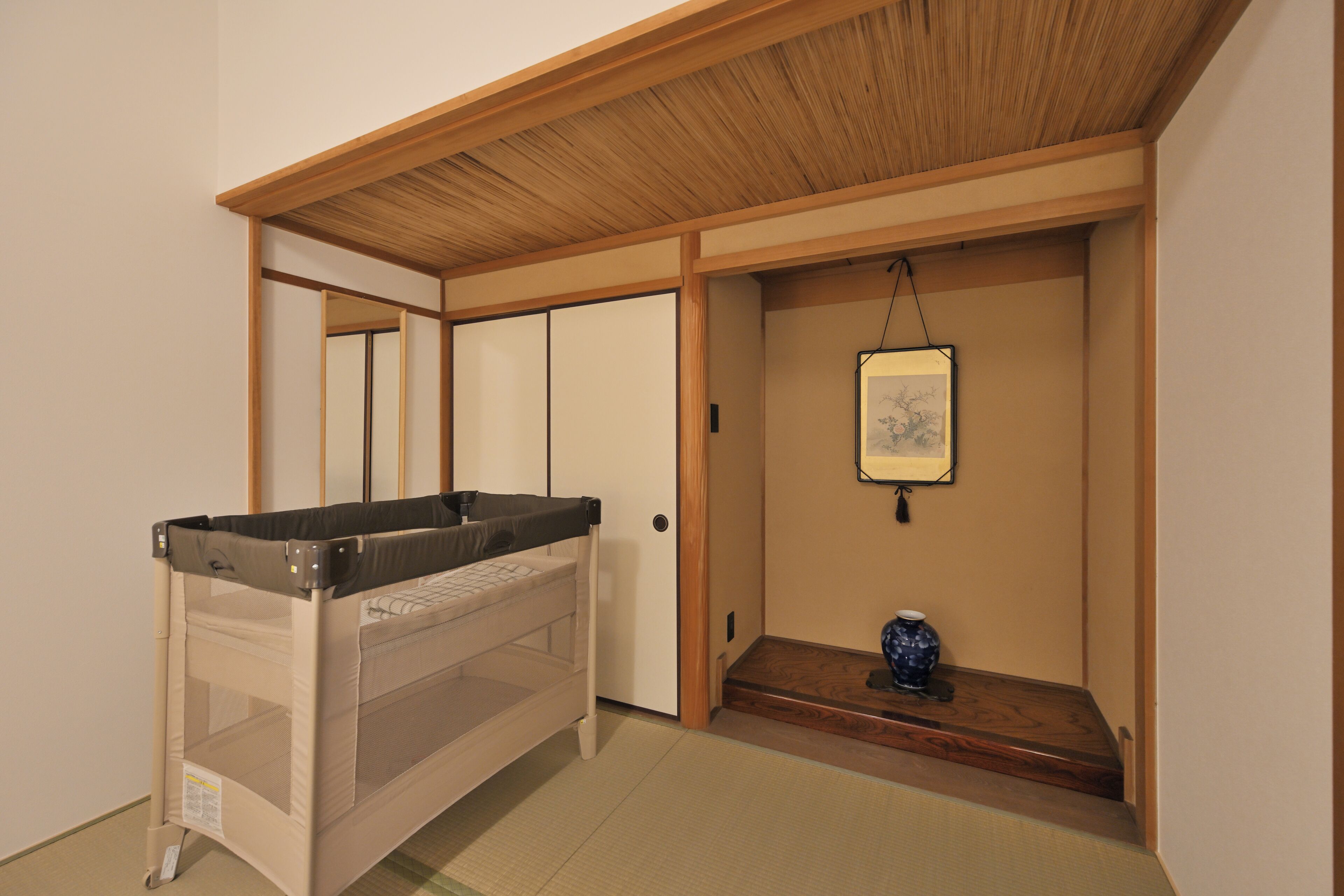A room with a bunk bed, tatami flooring, a wooden ceiling, a sliding door, and a small shelf with a vase.