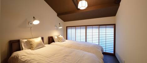 A bedroom with two beds, wooden beams on the ceiling, and a large window with blinds.