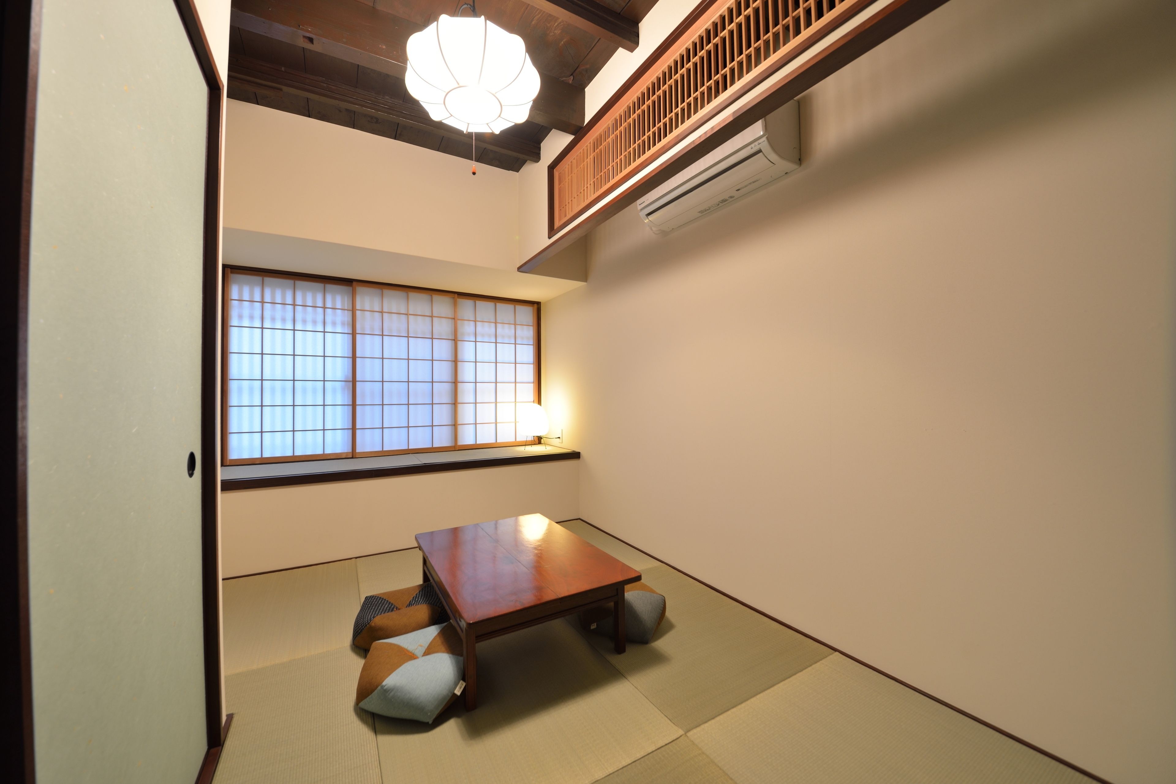 Una tradizionale stanza giapponese con pavimento in tatami, un tavolino in legno, cuscini e una finestra con paravento shoji.