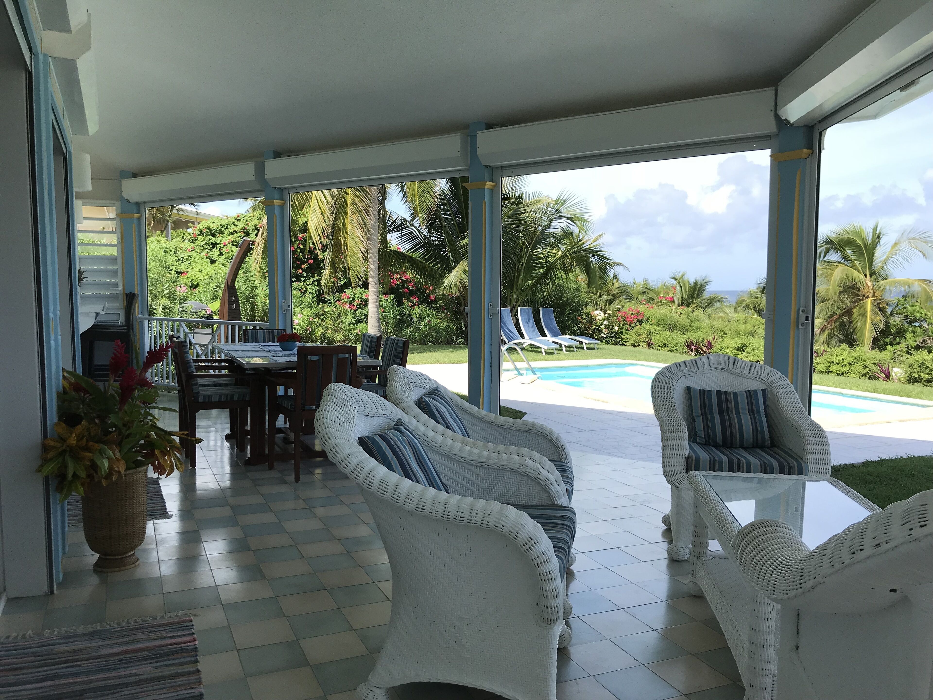 A covered outdoor area with wicker furniture, a pool, and lush greenery.