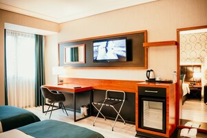 Una habitación de hotel con escritorio, dos sillas, televisor, minibar y cama.