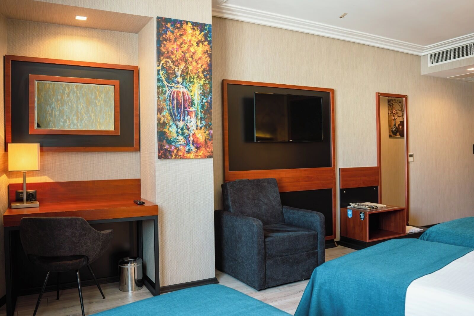 A hotel room with a desk, chair, TV, and two beds.