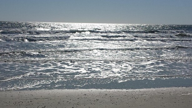 A beach with a clear sky and sunlight reflecting off the water.